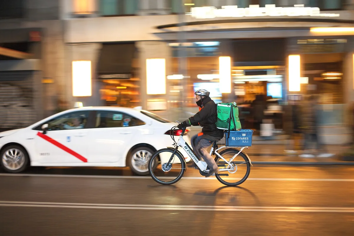 Kurýr na kole s batohem pro rozvoz jídla projíždí noční ulicí v rámci platformové práce