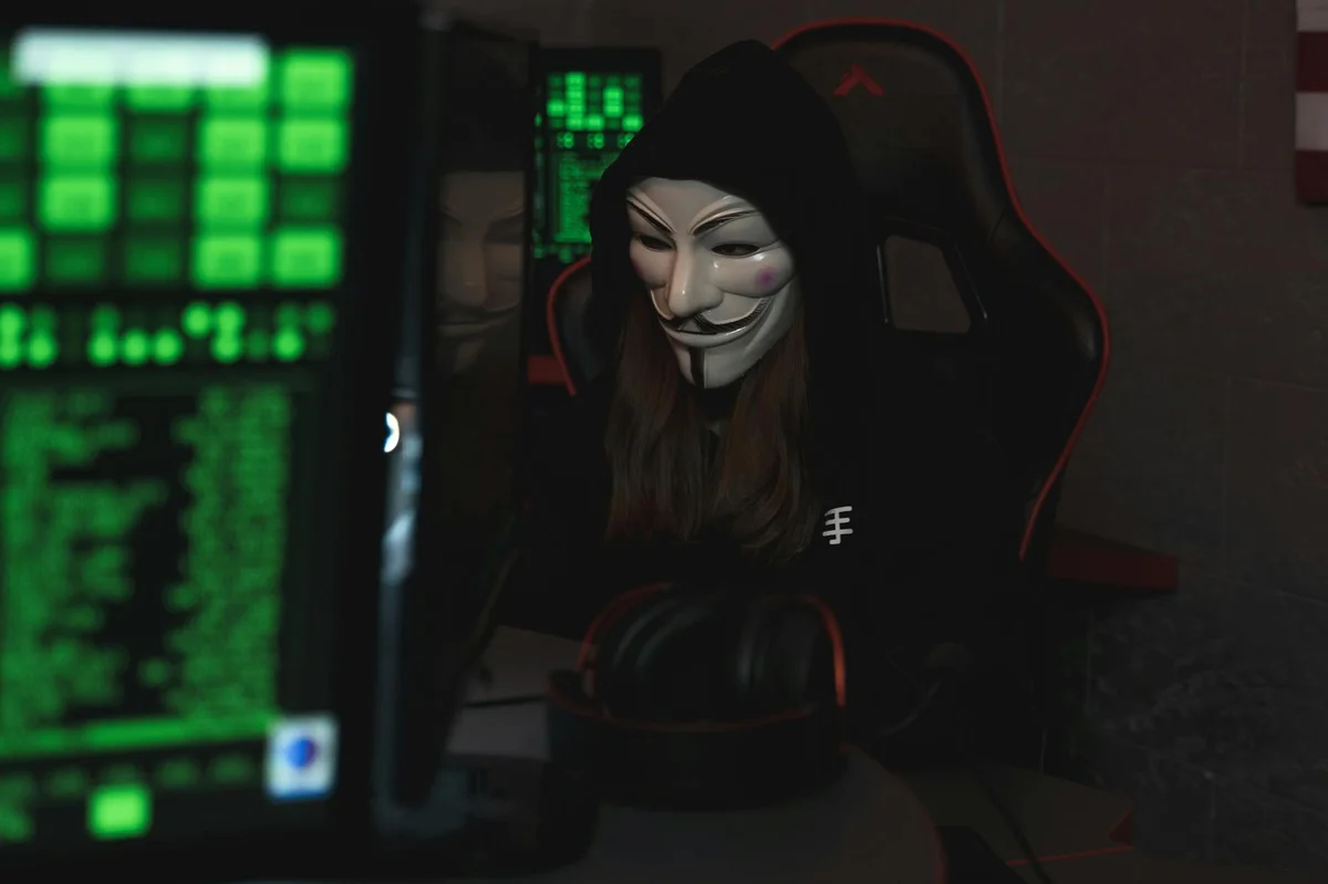 Phishing útok — anonymní hacker s maskou u počítače s kyberbezpečnostními daty