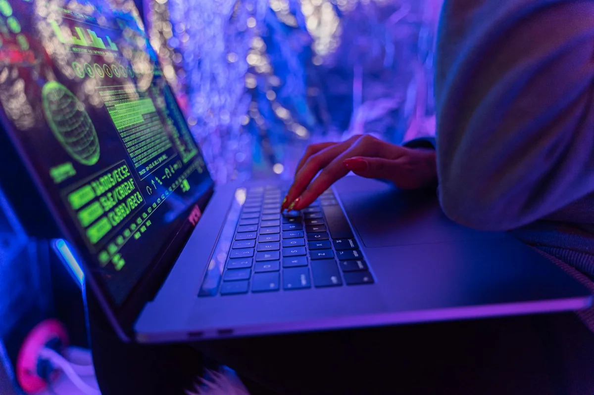 haker piszący na laptopie w ciemnym pokoju — phishing jak rozpoznać