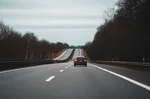 Auto jedoucí po evropské silnici mezi stromy za zataženého podzimního dne